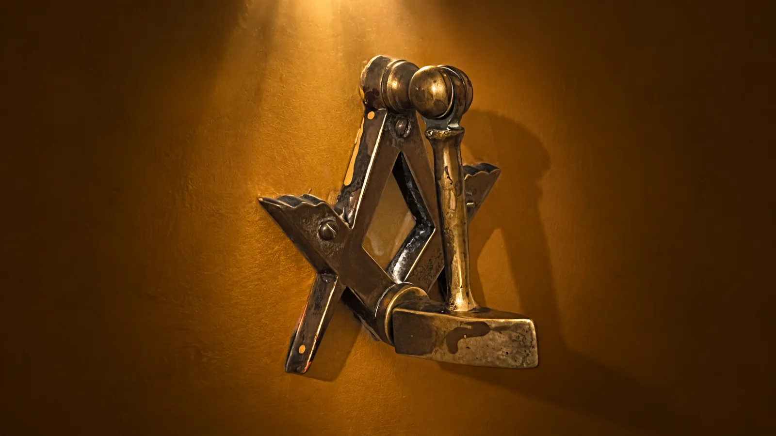 A brass door knocker cast in the form of the square and compasses.