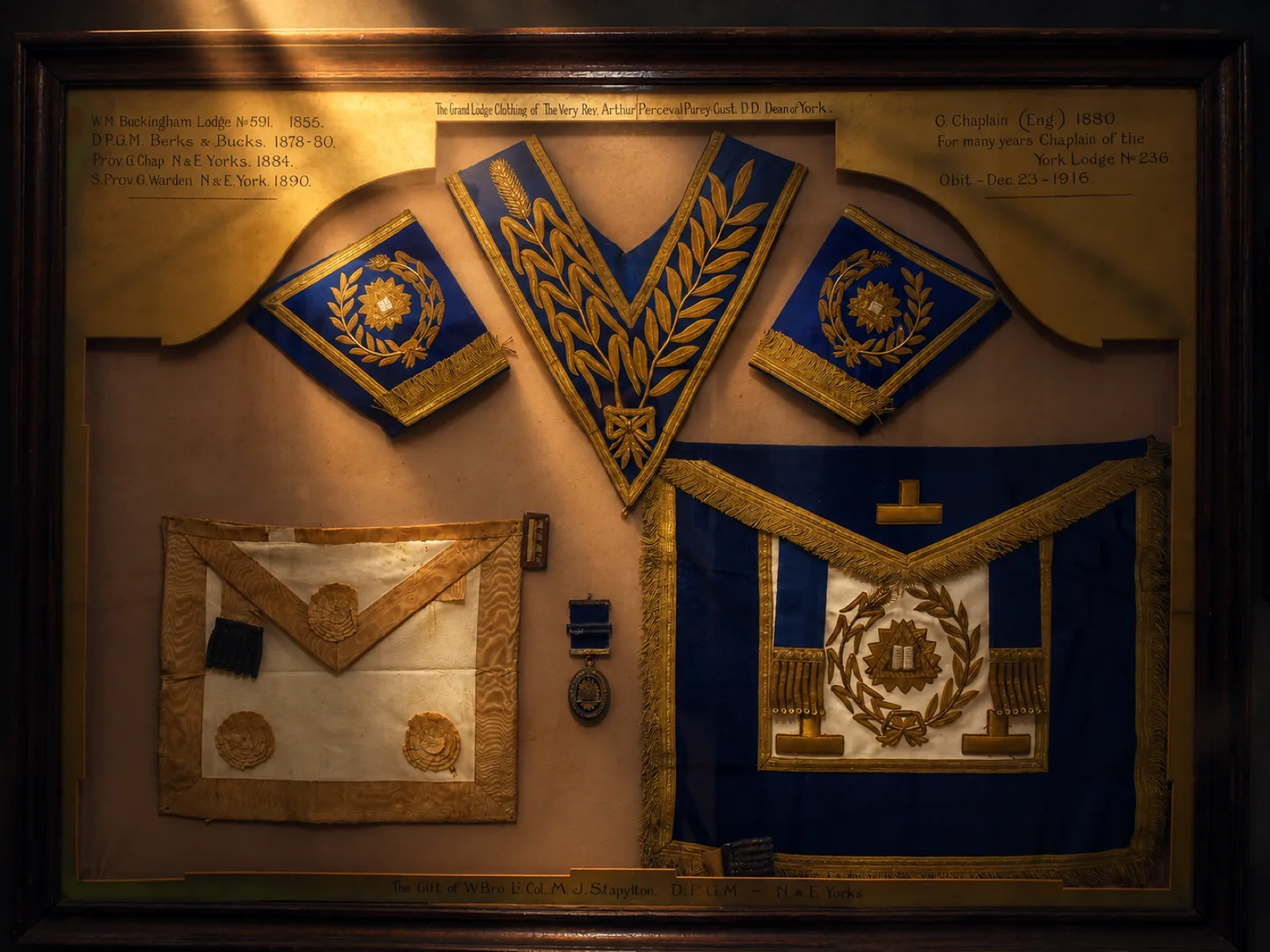 A framed case of historic Grand Lodge regalia, including collars, an apron and a jewel, presented in memory of a former Chaplain of the Lodge.
