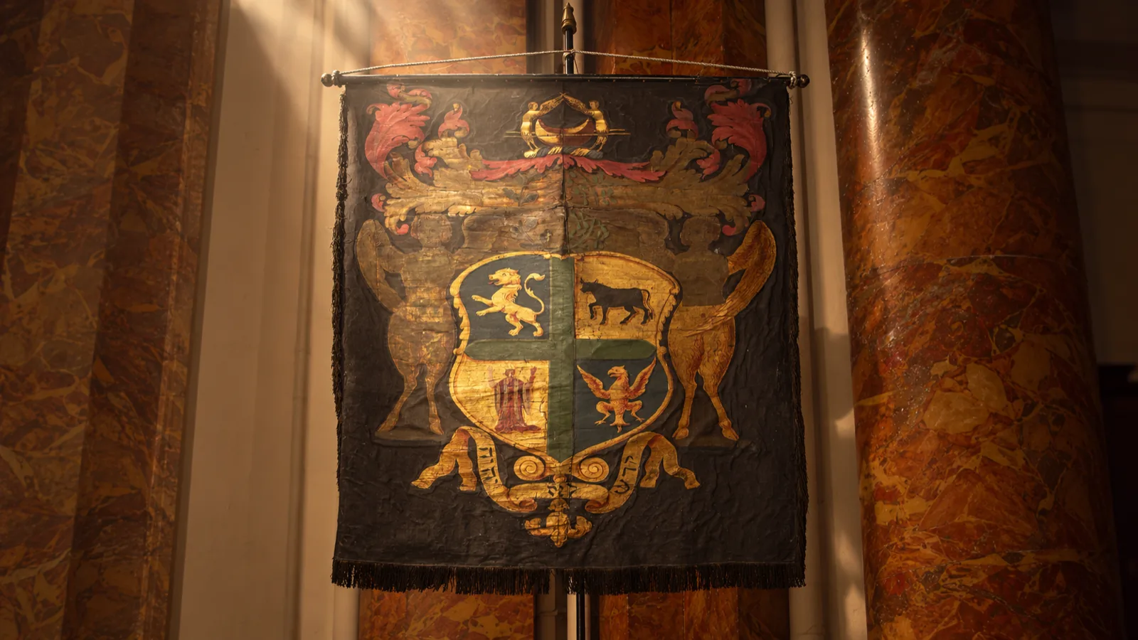 A heraldic ceremonial banner bearing a shield with a lion, bull and griffin.